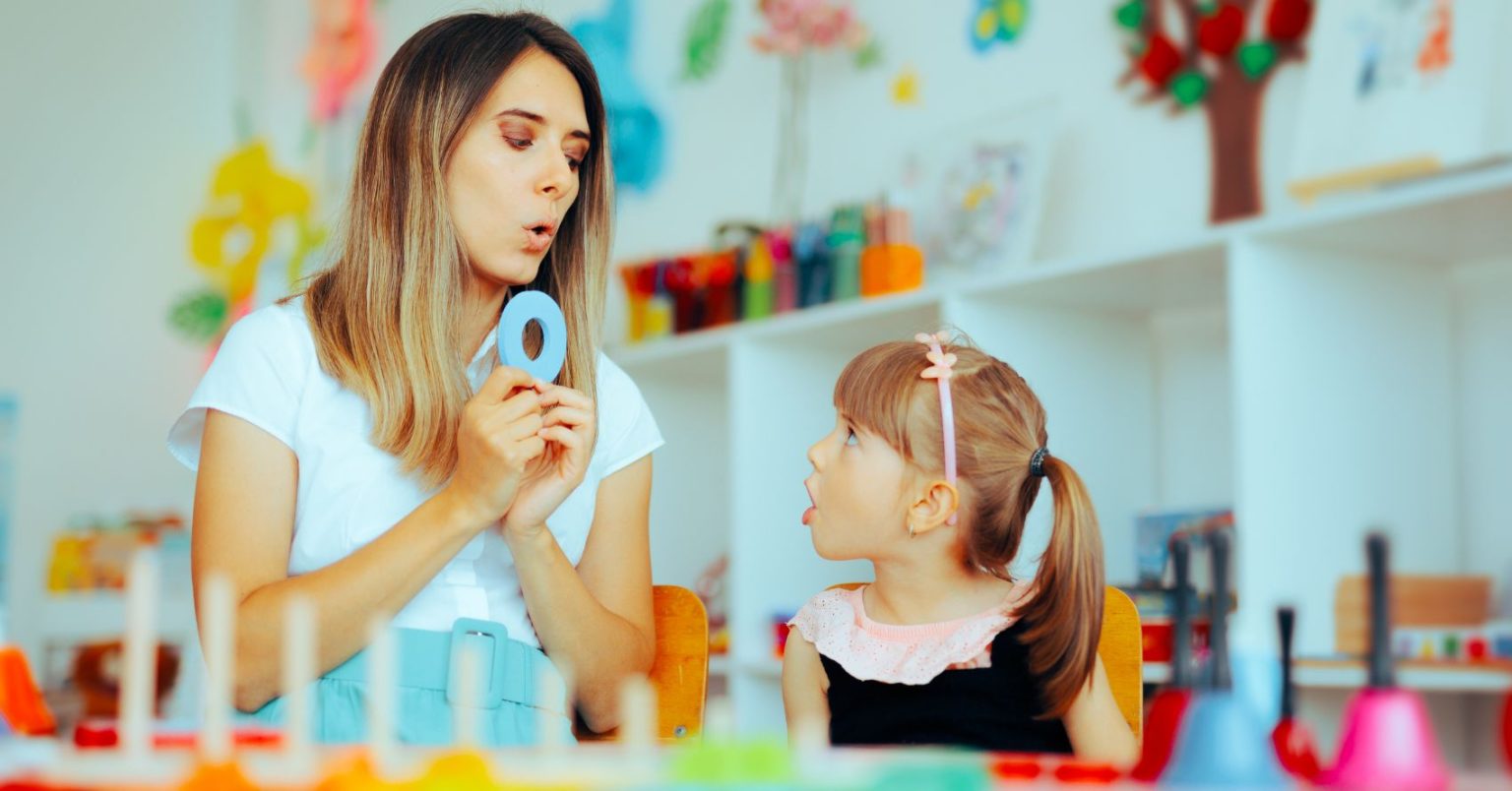 Speech pathologist supporting a young child during a therapy session.