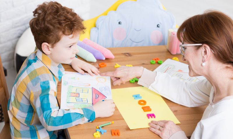 Speech pathologist supporting a young child during a therapy session using different resources.
